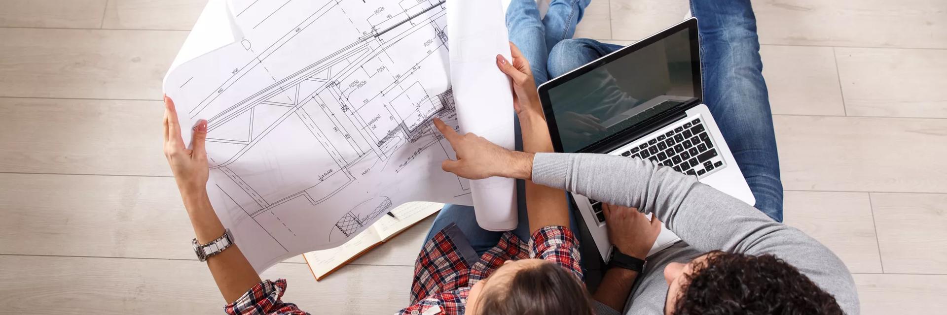 Young couple sitting on the floor and looking at the blueprint of new home.