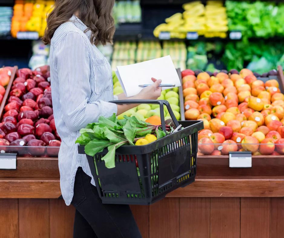 A woman observing a grocery store filled with a variety of fresh fruits and vegetables.