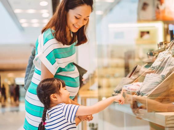 Lovely little daughter having window shopping with her young pregnant mom joyfully in the shopping mall