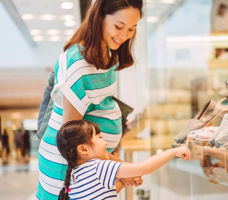 Lovely little daughter having window shopping with her young pregnant mom joyfully in the shopping mall