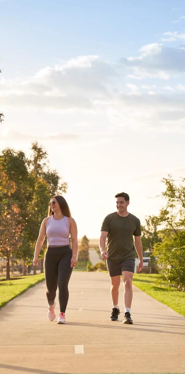 Two individuals jogging on a park path, surrounded by lush greenery and trees.