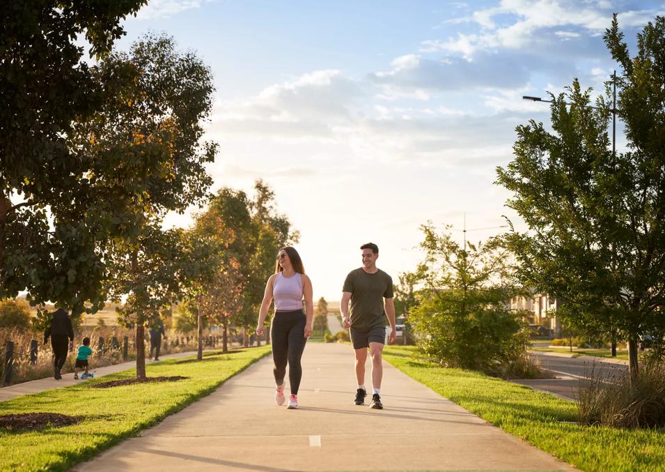 Two individuals jogging on a park path, surrounded by lush greenery and trees.